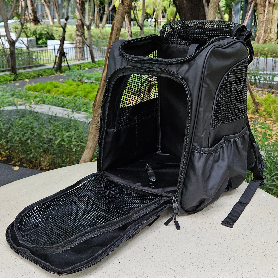 Black Pawbella pet backpack with open mesh zip compartment, showcased on a park table with natural greenery in the background.