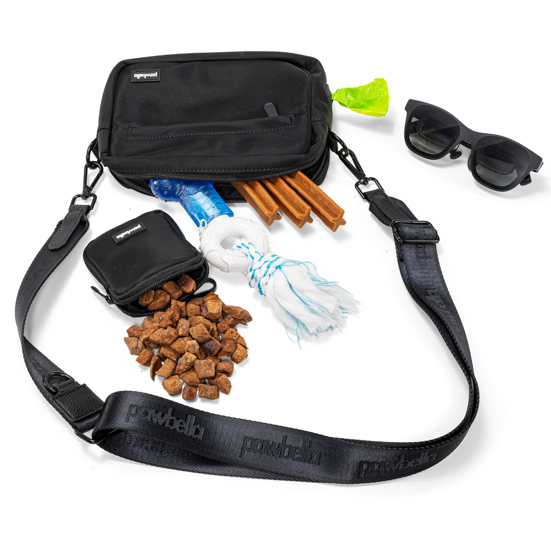 Pawbella dog walking shoulder bag in black, packed with accessories including dog treats, chew sticks, a toy, waste bags, and a compact pouch for pet essentials