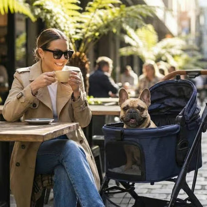 A woman in sunglasses and a trench coat enjoys coffee at an outdoor café in Australia as her French Bulldog relaxes nearby in the Pawbella Ultimate Pet Stroller with Detachable Carrier (up to 22kg). Lush green plants complete the cozy scene.