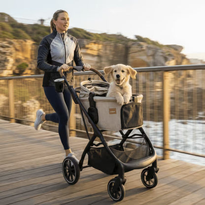 A woman jogs along a coastal boardwalk in Australia, pushing the Pawbella Ultimate Pet Stroller with Detachable Carrier (up to 22kg) by Pawbella, carrying a happy golden retriever puppy. Cliffs and ocean can be seen in the background.