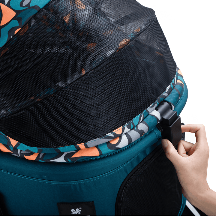 Detail view of the canopy mechanism on a teal pet stroller, showing the mesh cover and patterned fabric, with a hand adjusting the lock.